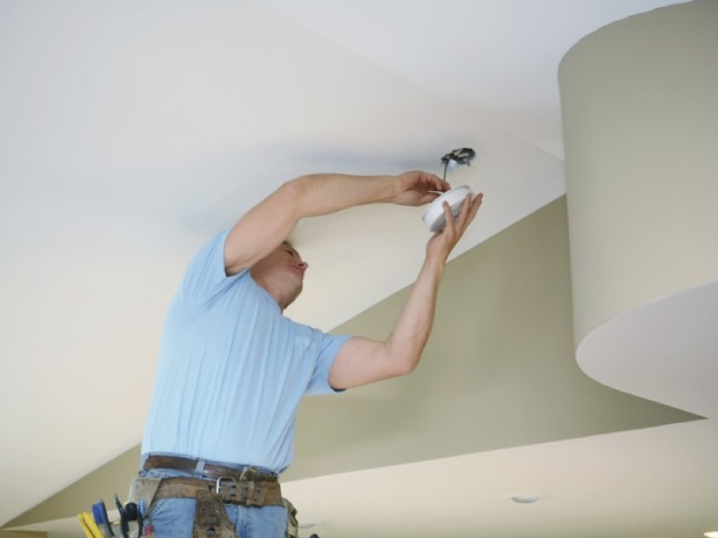 Un homme installe un détecteur de fumée électrique au plafond d'une résidence